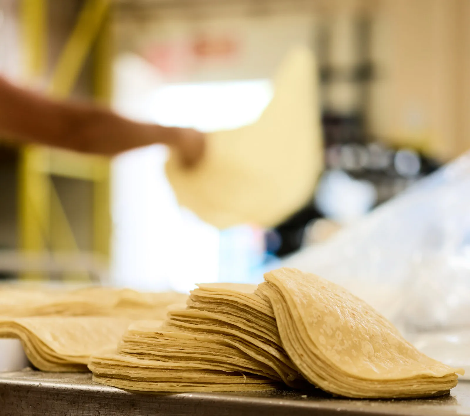 Una pila de tortillas de maíz en una charola, con una mano levantando una detrás